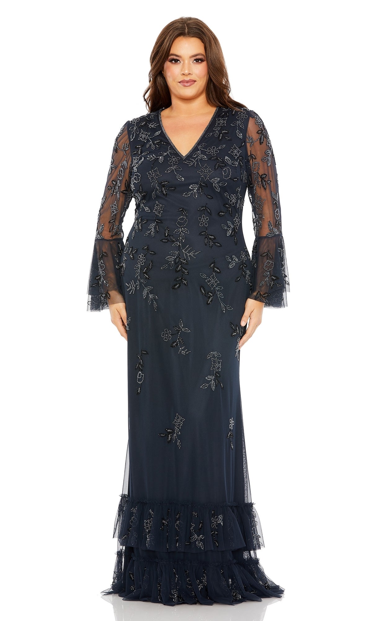 A woman stands facing forward in the Long Plus-Size Formal Dress 9239 by Mac Duggal, a midnight blue gown with sheer embroidered long sleeves and floral embellishments.